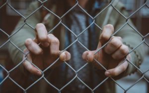 Hands gripped around a chain-link fence.