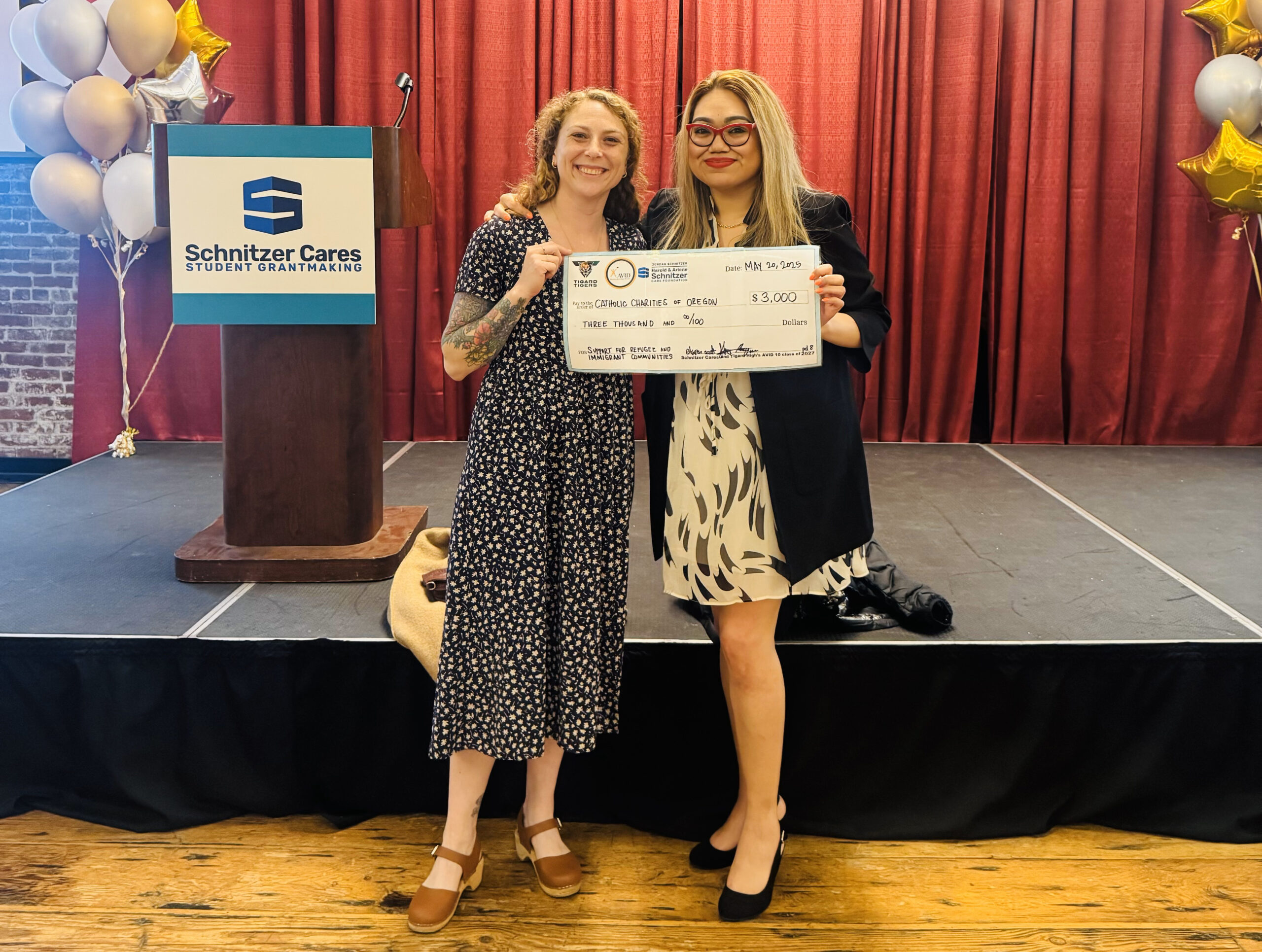 Claire McIlwain and Claudia Munoz of the Catholic Charities of Oregon refugee resettlement program hold a check for the agency given by the Schnitzer Cares Foundation and students from Tigard High School.
